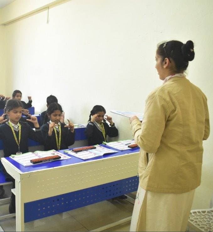 Mastermind teacher leading an abacus and mental-maths session with students at their desks in a partner school classroom