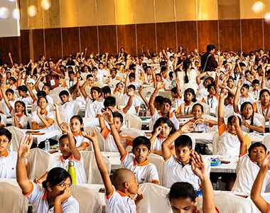 A packed classroom of Mastermind Abacus students raising their hands
